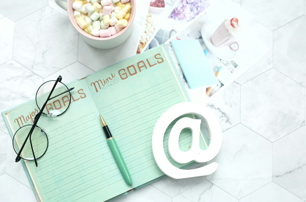 Person writing goals in a journal near a laptop for personal development
